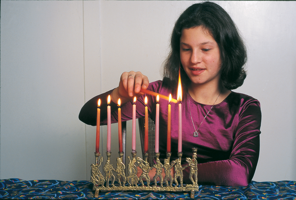 A girl lights hanukkiyah candles to celebrate Hanukkah