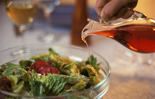 Pouring red wine vinegar on a salad